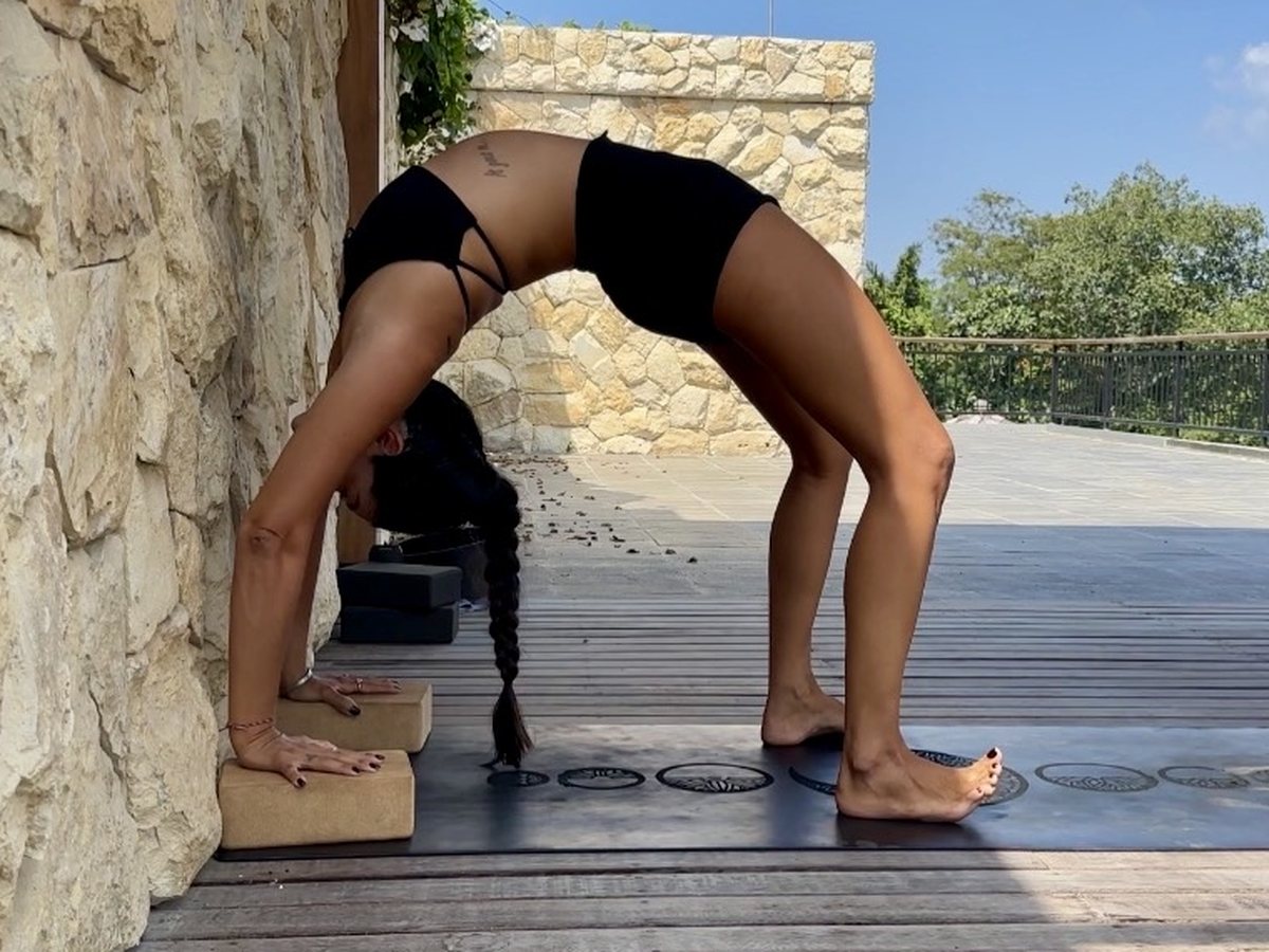 Irene in wheel pose with her hands on blocks against a stone wall