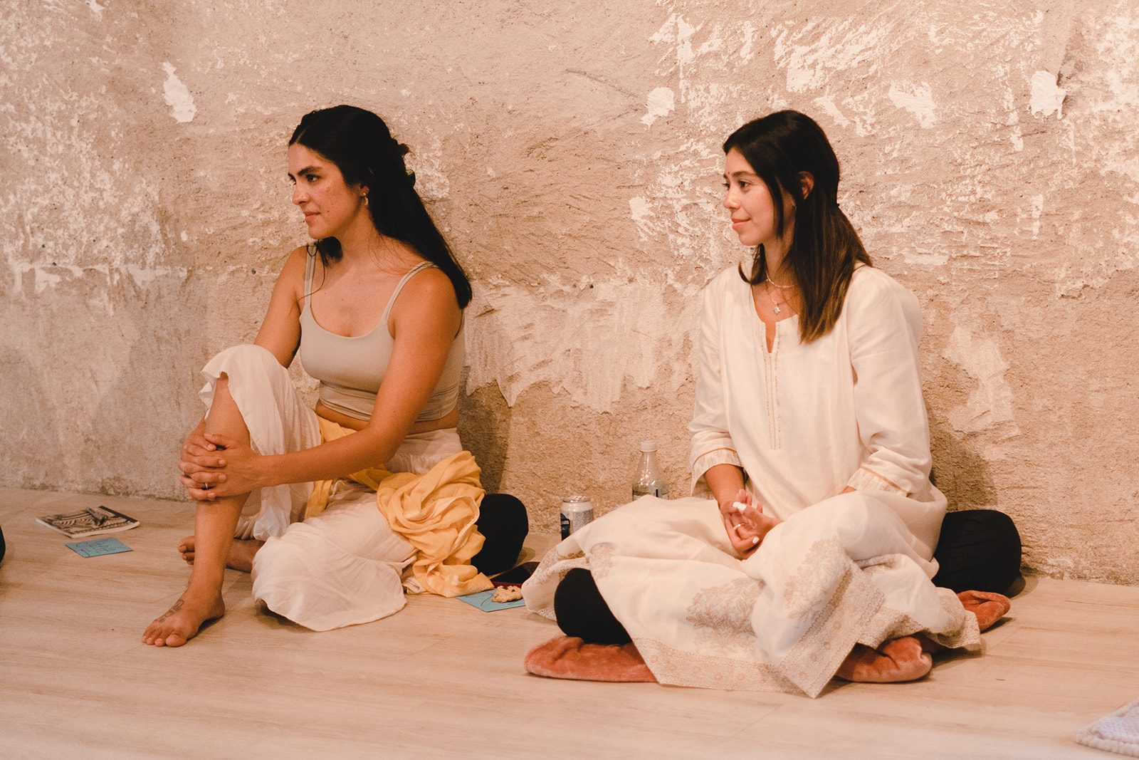Two women dressed in white sitting against a rustic plaster wall at a women's yoga immersion in Antigua Guatemala
