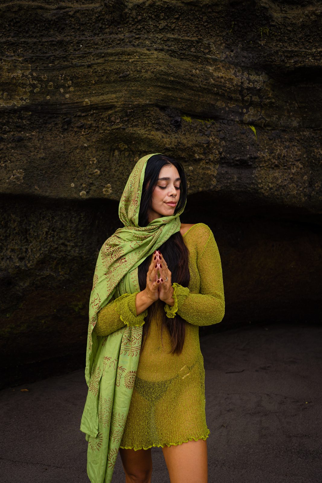 Irene del Valle in an olive green dress with hands in prayer on black volcanic rock in Bali